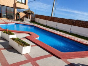 Piscina con borde rojo, rodeada por un muro blanco y una valla de madera.