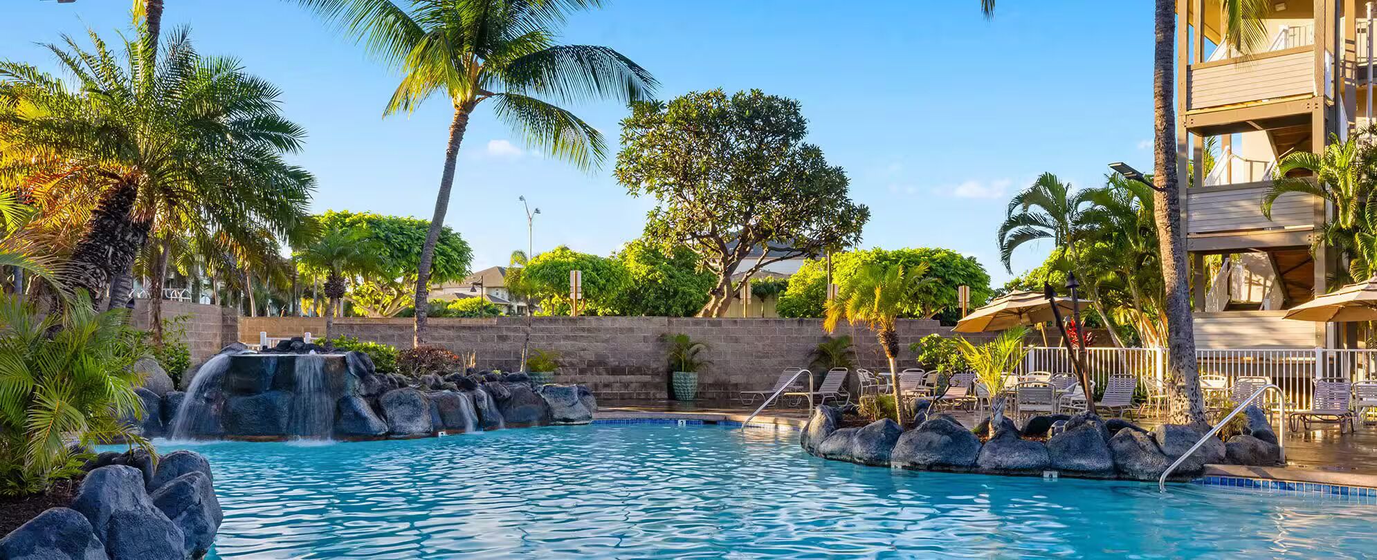 A pool with a waterfall feature, surrounded by palm trees and lounge chairs.