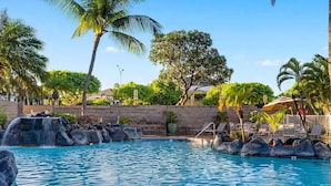Una piscina con cascada, rodeada de palmeras y sillas de descanso.