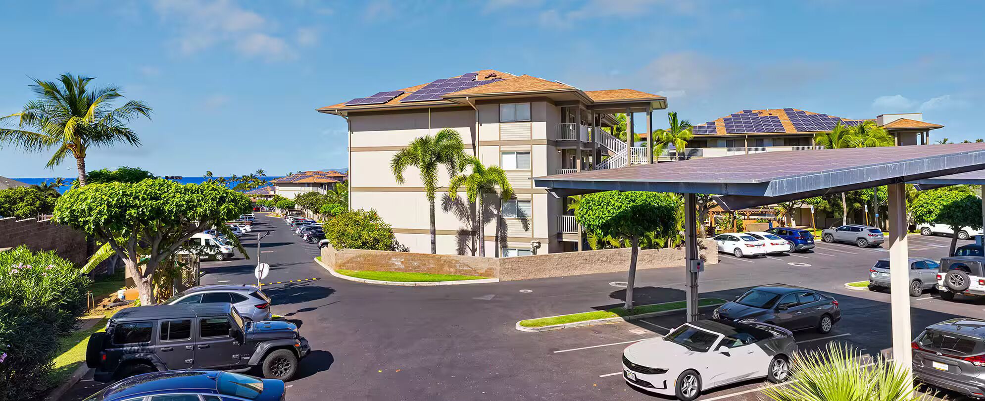 A parking lot with multiple cars, a building with solar panels, and a covered area with a roof.
