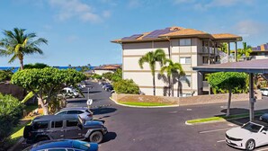 Un estacionamiento con varios autos, un edificio con paneles solares y un área cubierta con techo.