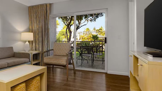 Una sala de estar con sofá, mesa de centro, televisor, lámpara, silla y un balcón con mobiliario exterior.