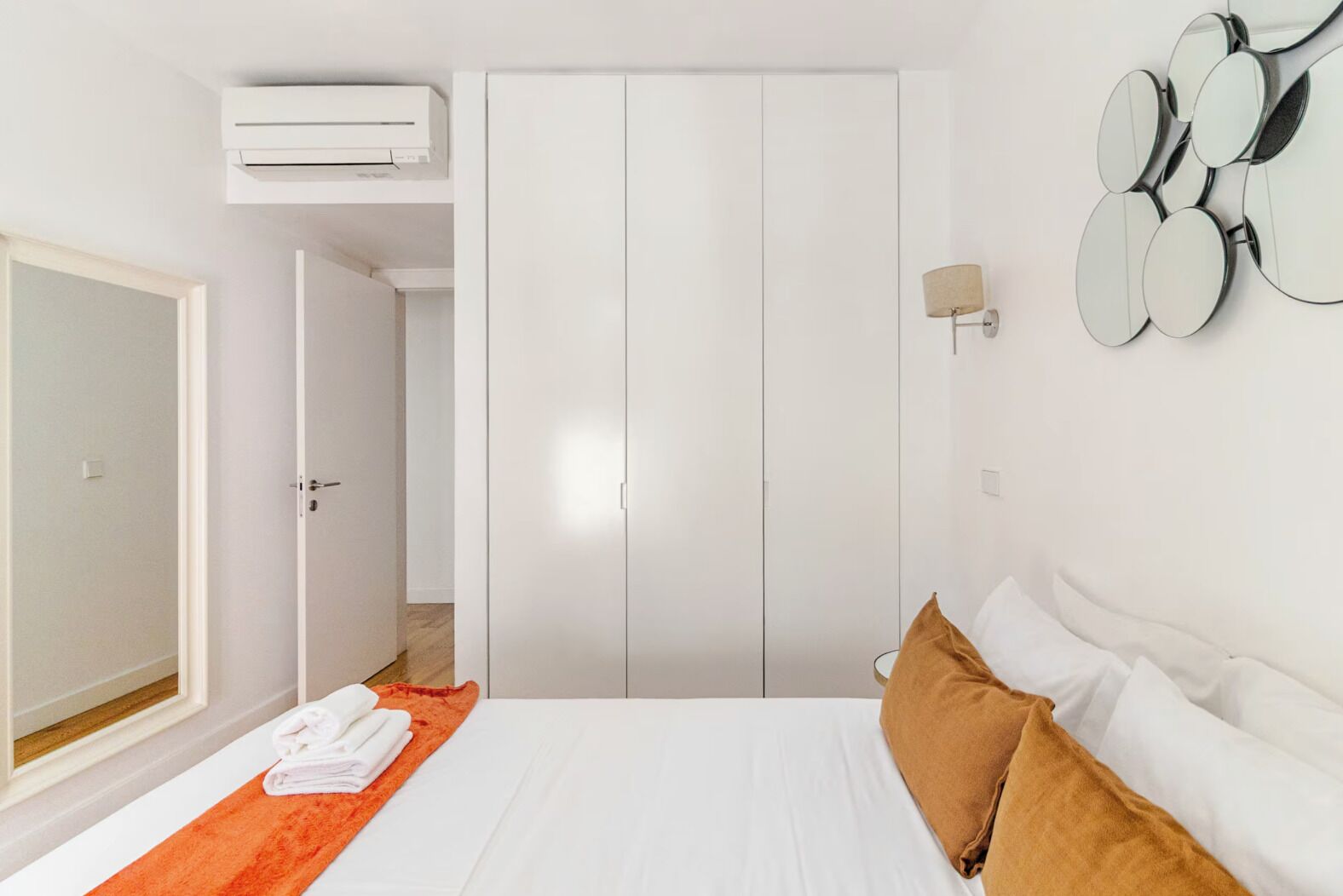 Una habitación de hotel con una cama, un equipo de aire acondicionado, un armario y un espejo montado en la pared.