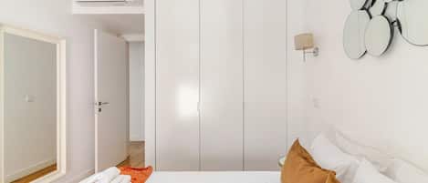Una habitación de hotel con una cama, un equipo de aire acondicionado, un armario y un espejo montado en la pared.