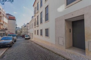 Eine enge Kopfsteinpflasterstraße, gesäumt von mehrstöckigen Gebäuden, parkenden Autos und einer Tür auf der rechten Seite.