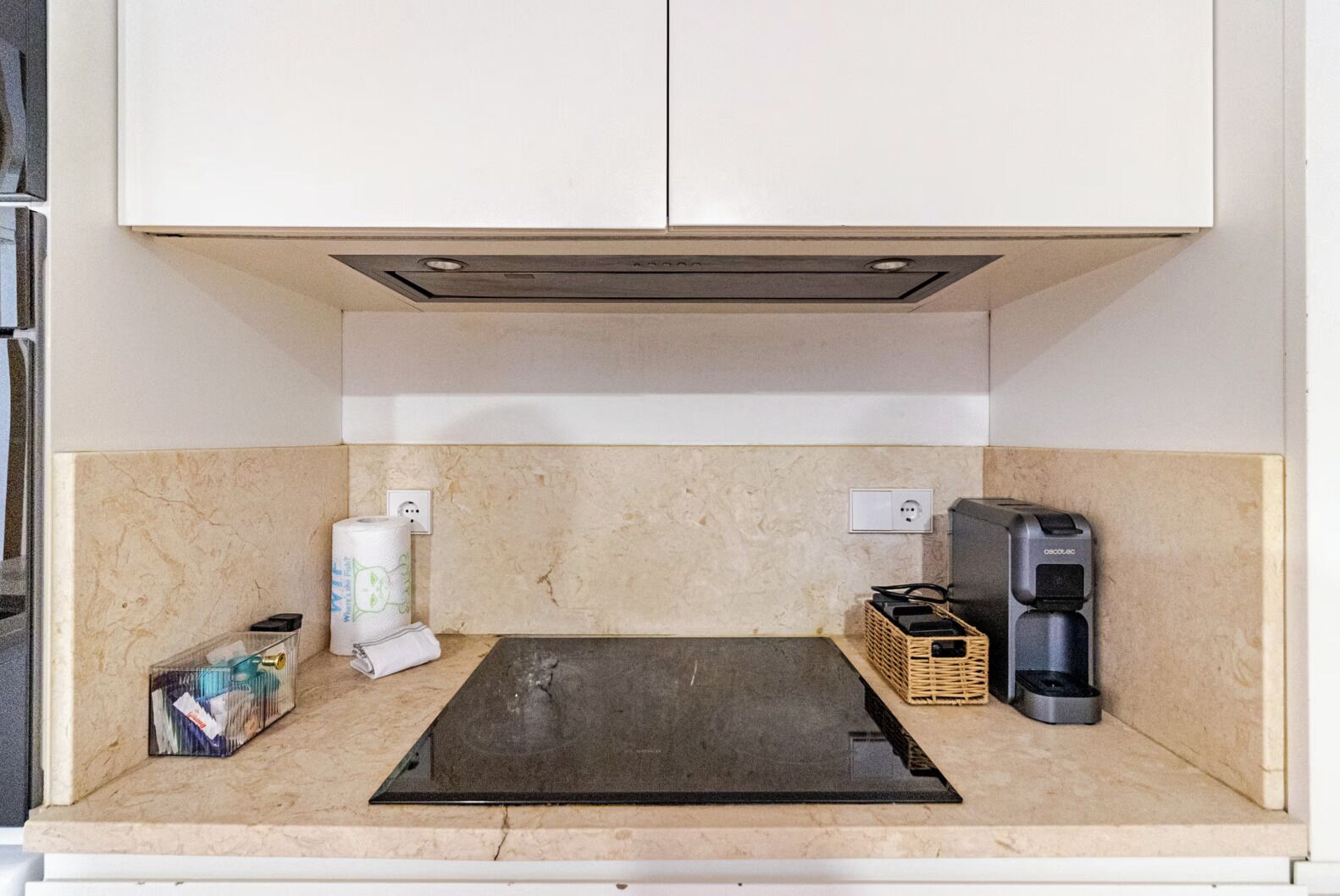 A kitchenette with a black induction cooktop, a coffee maker, a basket, and a roll of paper towels.
