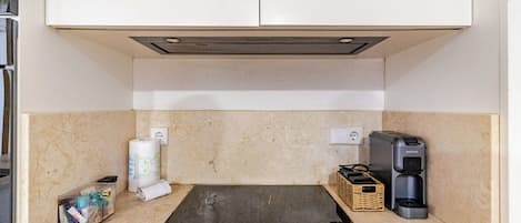 A kitchenette with a black induction cooktop, a coffee maker, a basket, and a roll of paper towels.