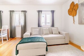 Ein modernes Wohnzimmer mit Sofa, Sessel, Couchtisch und einer Wanddekoration mit Blättern.
