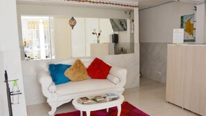 A white sofa with colorful pillows, a small white coffee table, and a colorful rug in a room with a white cabinet and a map on the wall. - Hostal Marbella 47 (Cartagena)