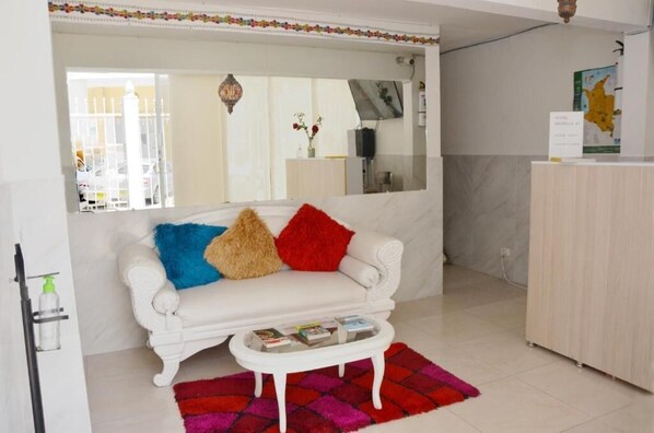 A white sofa with colorful pillows, a small white coffee table, and a colorful rug in a room with a white cabinet and a map on the wall.