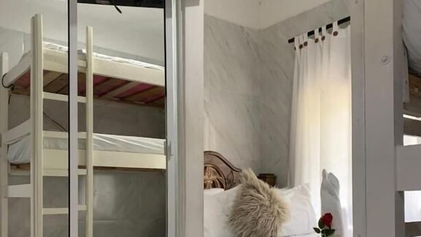 A bedroom with a bunk bed, a glass door leading to another room, a bed with a white comforter, a fluffy pillow, and a single red rose. - Hostal Marbella 47 (Cartagena)