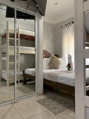 A bedroom with a bunk bed, a glass door leading to another room, a bed with a white comforter, a fluffy pillow, and a single red rose.