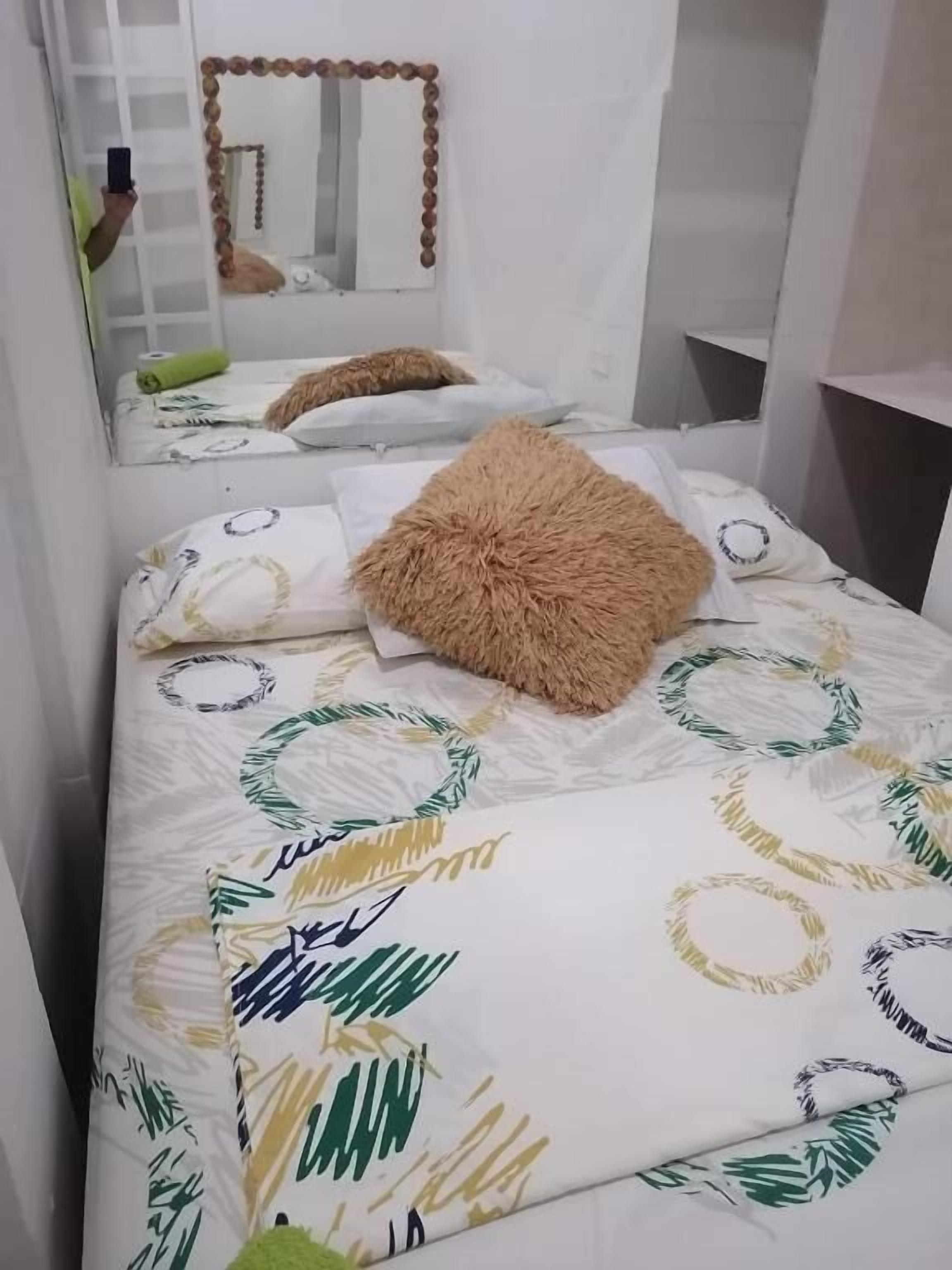 A bedroom with a bed, pillows, a fluffy pillow, a mirror, and a shelf.
