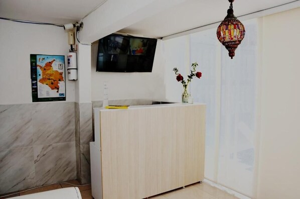 A reception area with a marble wall, a wooden reception desk, a wall-mounted TV, and a decorative hanging light.