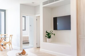 A modern living room with a flat-screen TV mounted on the wall, a round wooden table with chairs, and a potted plant. - The Chapter - Luxury Harbour Apt - Newcastle East (Newcastle)