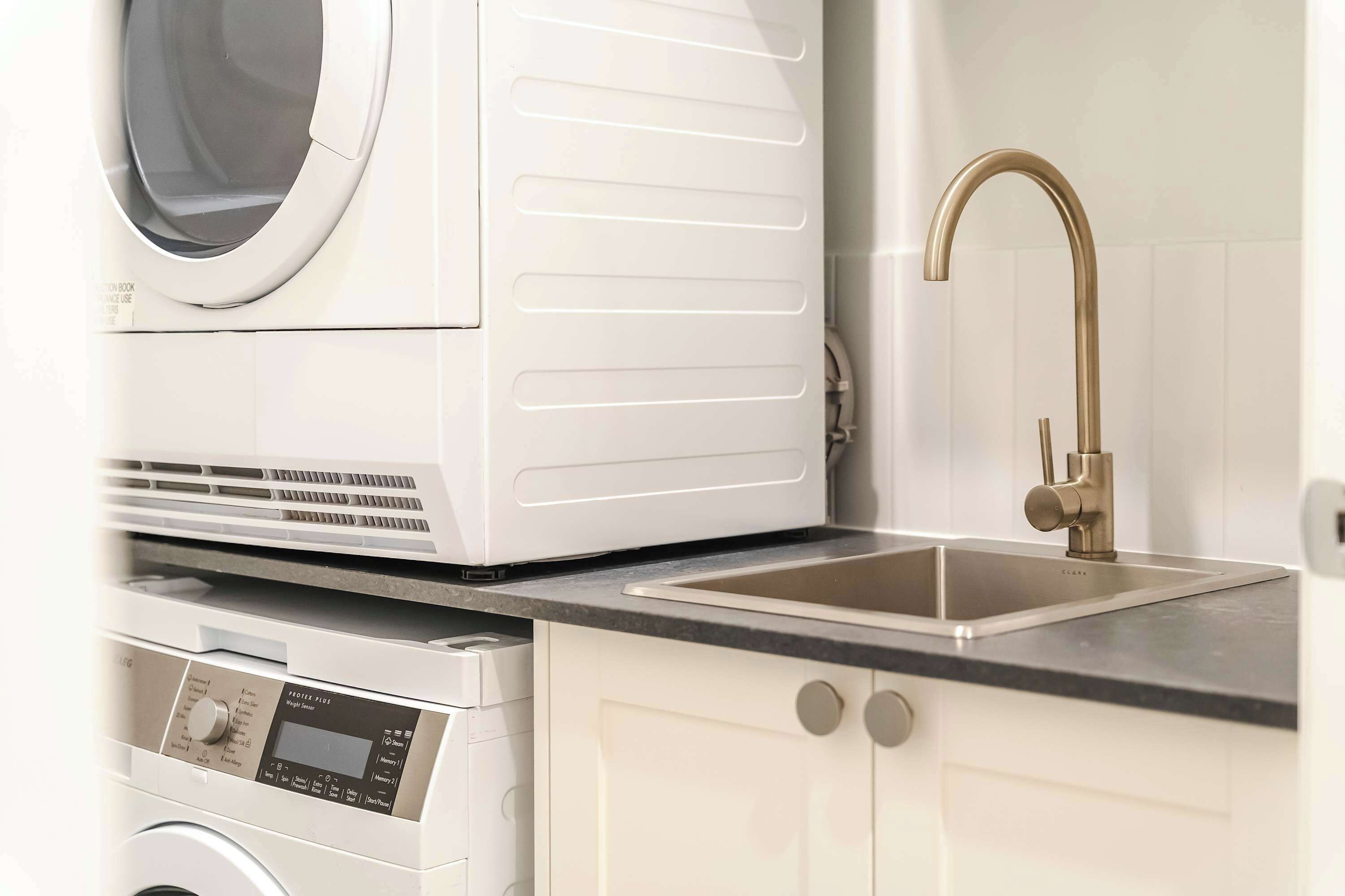 A compact kitchen with a washing machine, a sink with a gold faucet, and a digital control panel.