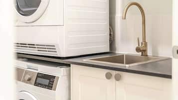 A compact kitchen with a washing machine, a sink with a gold faucet, and a digital control panel.