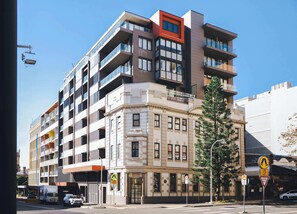 A multi-story building with a mix of modern and classic architectural styles, featuring balconies and a ground-level entrance. - The Chapter - Luxury Harbour Apt - Newcastle East (Newcastle)
