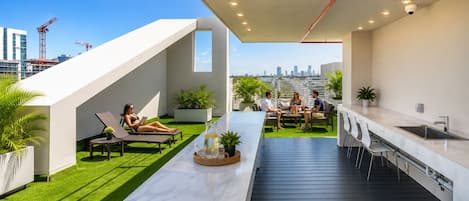 A rooftop terrace with a long table, seating areas, and a city skyline view.