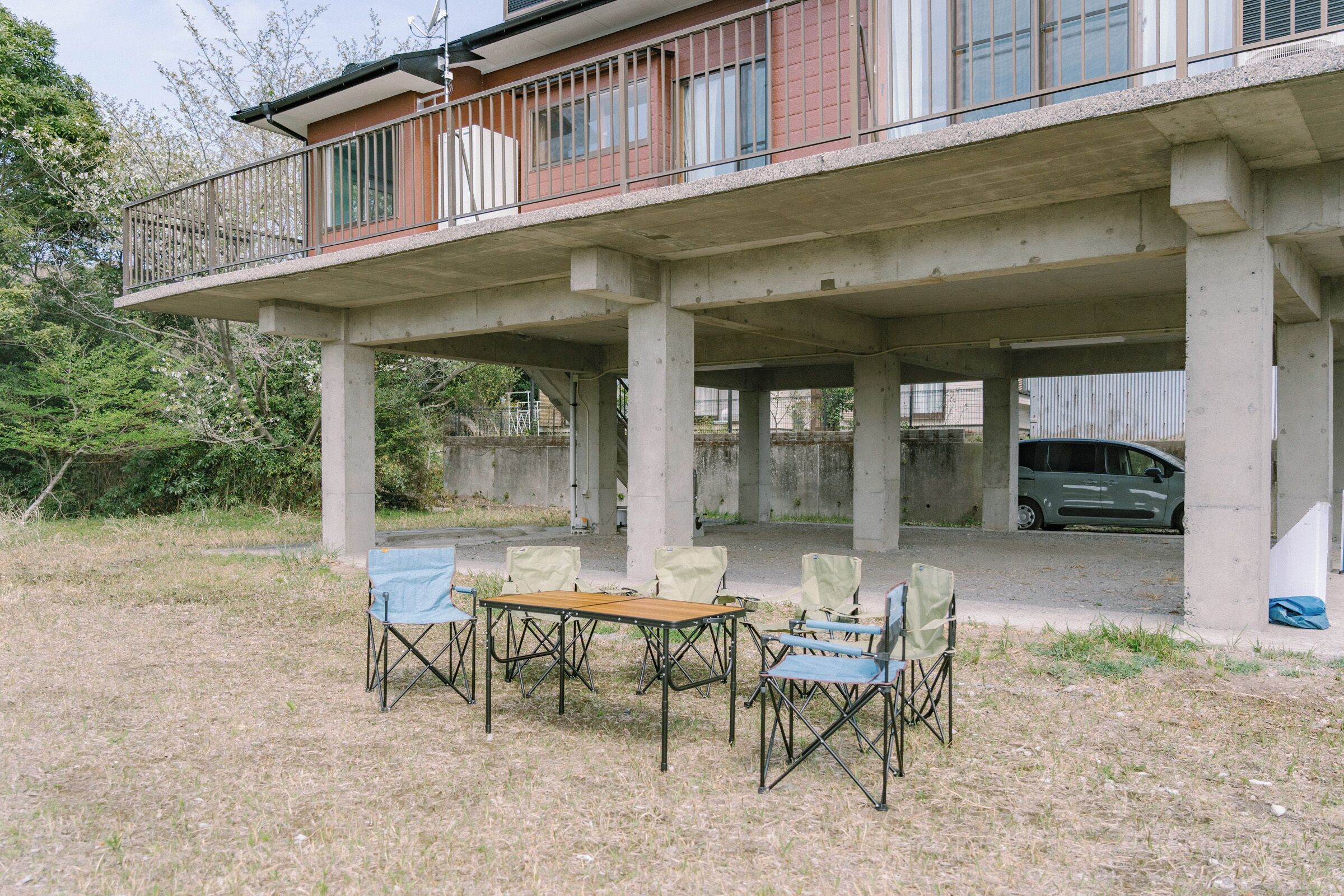 A building with a balcony, concrete pillars, and a table with chairs.