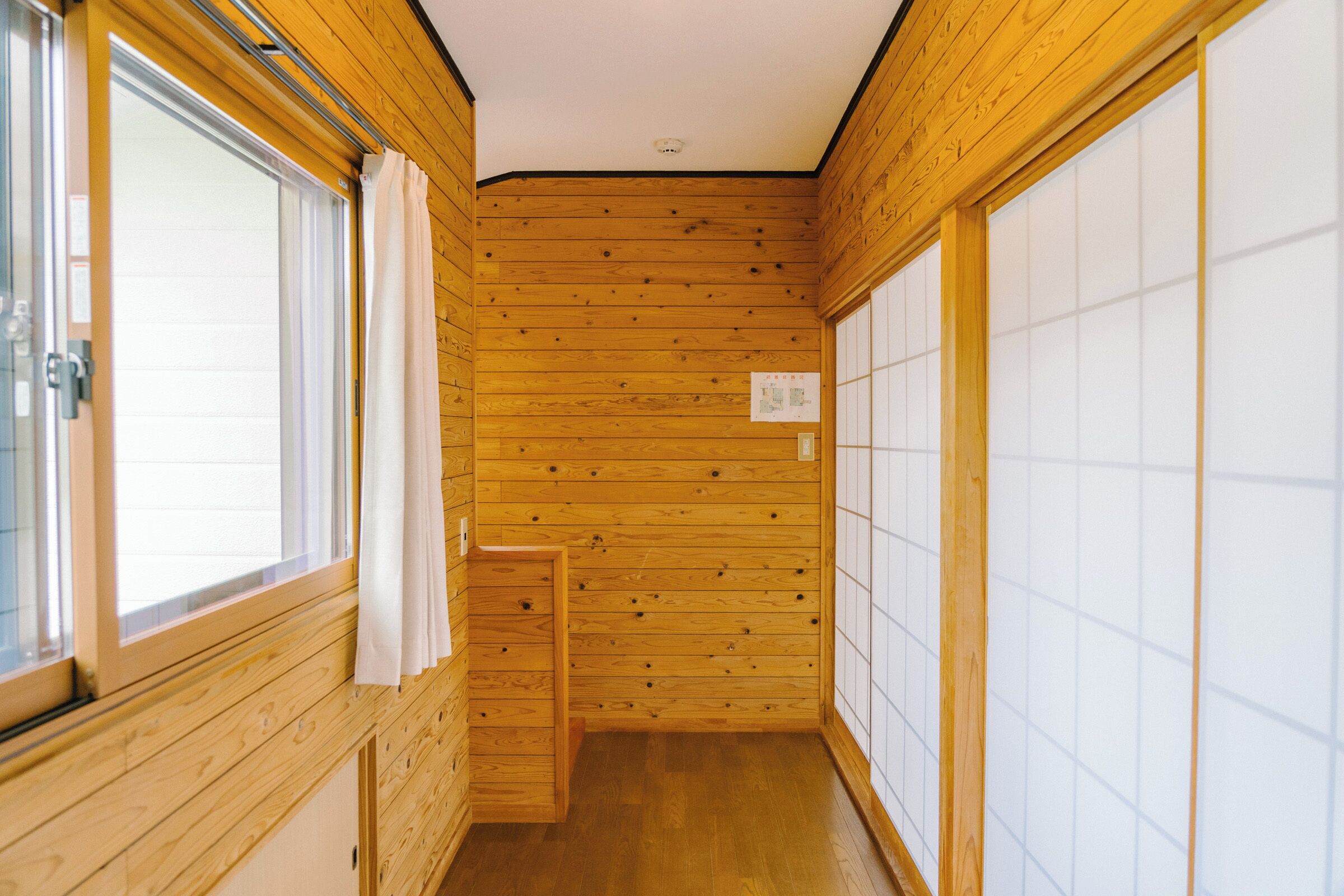 A narrow hallway with wooden walls and a wooden floor, leading to a sliding door on the right.