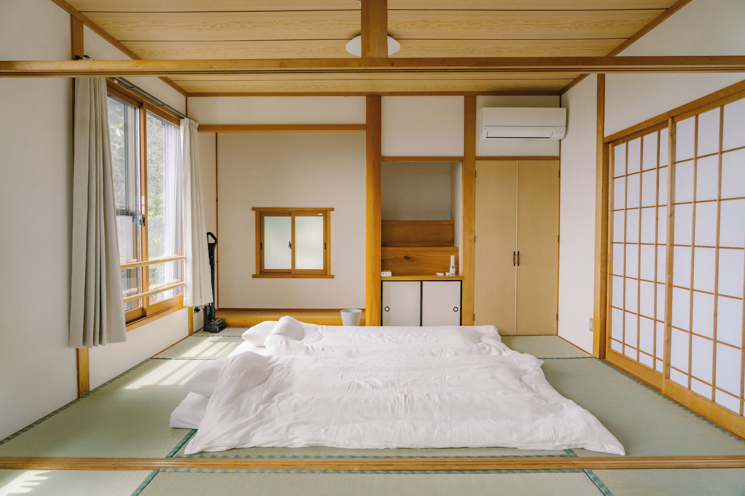A traditional Japanese room with tatami flooring, a bed with white bedding, a sliding door, and a window with curtains.