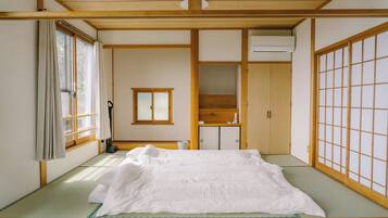 A traditional Japanese room with tatami flooring, a bed with white bedding, a sliding door, and a window with curtains.