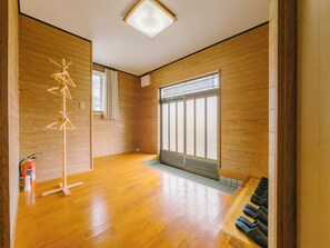Ein Zimmer mit Holzboden, Deckenleuchte, Fenster mit Blick und Schuhregal.
