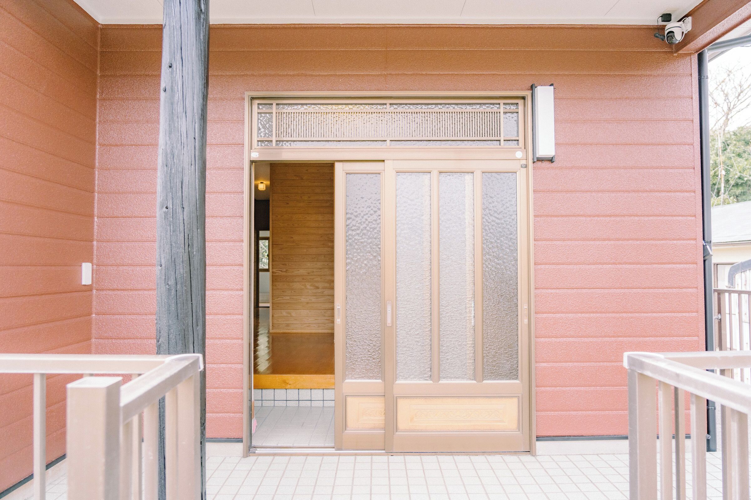 A sliding glass door entrance to a room with a wooden interior, a small window above the door, and a security camera on the wall.
