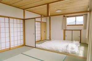 A traditional Japanese room with tatami flooring, sliding doors, and a bed with white bedding.