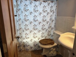 Un baño con inodoro, lavabo y cortina de ducha estampada con hojas.