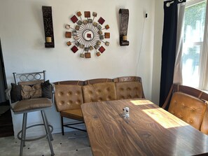 Una habitación con una mesa de comedor de madera, un sofá de cuero, un taburete de metal y un adorno en la pared.