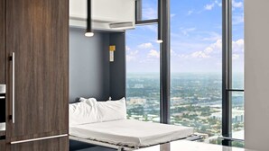 Quarto de hotel moderno com cama, vista da cidade e uma janela grande.