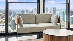 Uma sala de estar moderna com um sofá e uma mesa de centro redonda, grandes janelas com vista para a cidade.