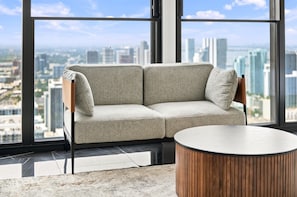 Ein modernes Wohnzimmer mit einer Couch und einem runden Couchtisch, große Fenster mit Blick auf die Stadt.