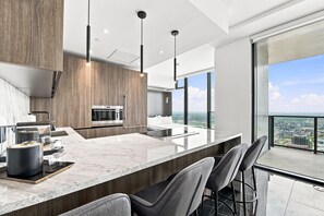 A modern kitchen with a large island, bar stools, and a city view through large windows. - Luxury Sky Penthouse with Ocean & City Views (Miami)