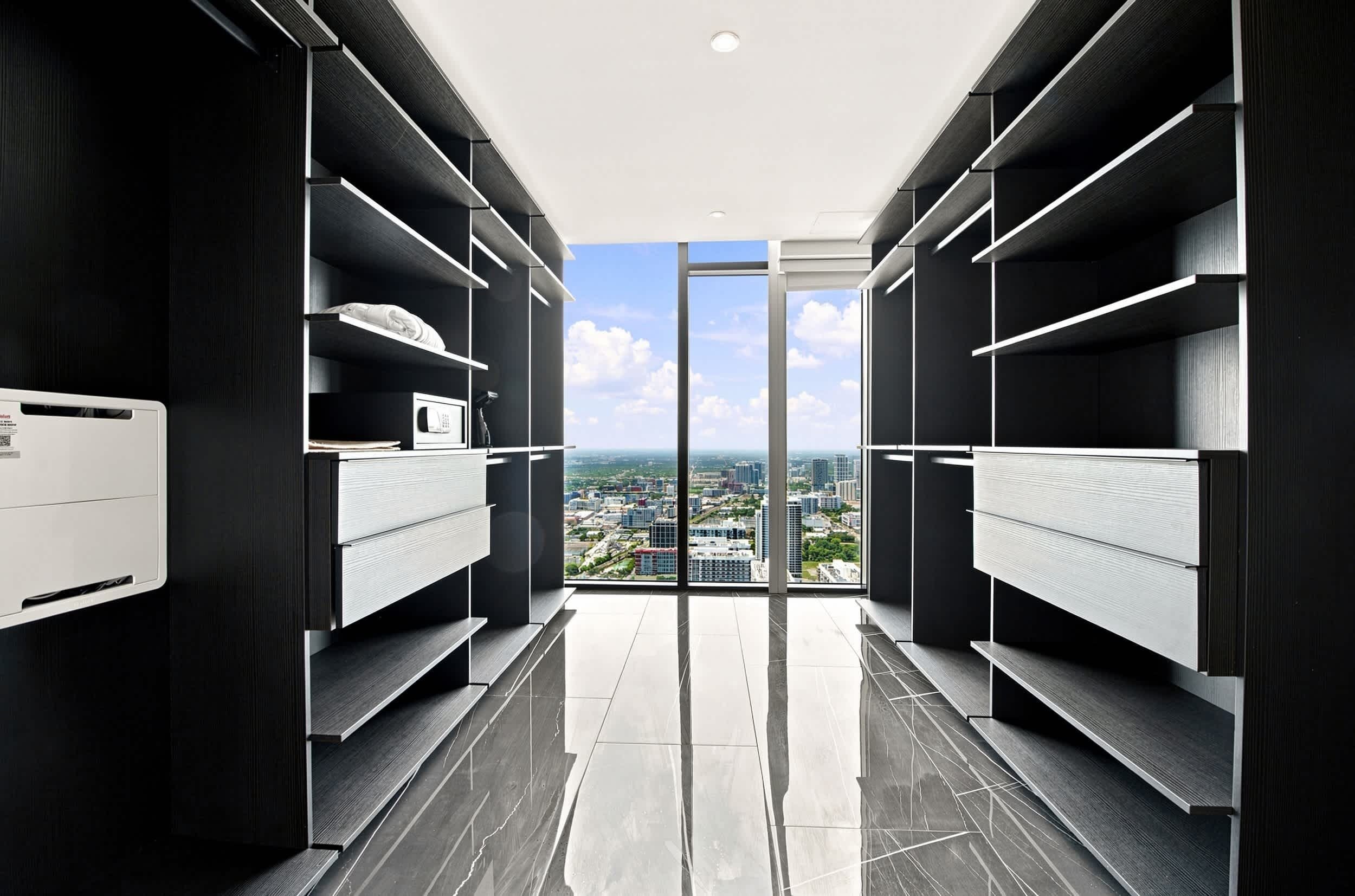 A modern closet with built-in shelving and a view of a cityscape through a glass door.