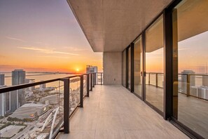 A balcony with a view of the sunset over a river, modern buildings, and a glass railing. - Luxury Sky Penthouse with Ocean & City Views (Miami)