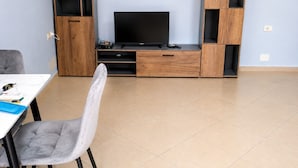 A modern living room with a TV, wooden entertainment unit, and a dining area with a table and chair. - A holiday home in a quiet neighborhood 5 minutes walking distance from the sea. (Vlora)