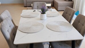 A dining area with a white table, grey upholstered chairs, and a grey sofa in the background. - A holiday home in a quiet neighborhood 5 minutes walking distance from the sea. (Vlora)