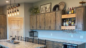 A kitchen with wooden cabinets, a granite countertop, a built-in island, and a refrigerator with beverages. - Lake home retreat in the heart of Okoboji (Milford)