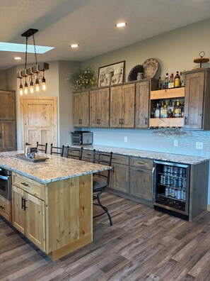 A kitchen with wooden cabinets, a granite countertop, a built-in island, and a refrigerator with beverages. - Lake home retreat in the heart of Okoboji (Milford)