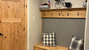 A wooden bench with checkered pillows, a metal rack with hooks, and a small American flag on a shelf. - Lake home retreat in the heart of Okoboji (Milford)