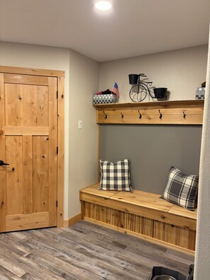 A wooden bench with checkered pillows, a metal rack with hooks, and a small American flag on a shelf. - Lake home retreat in the heart of Okoboji (Milford)