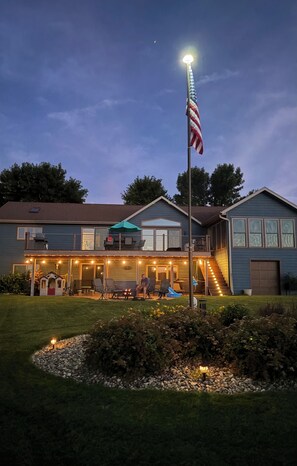 A residential house with a front deck, outdoor seating, and a flagpole. - Lake home retreat in the heart of Okoboji (Milford)