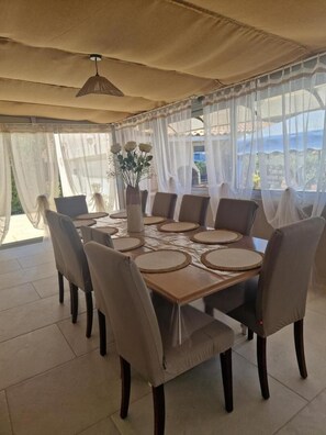 Comedor con una mesa dispuesta para seis personas, rodeada de sillas, bajo un dosel con cortinas traslúcidas.