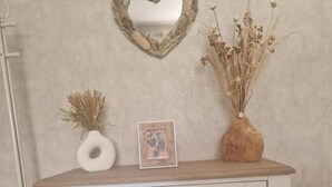 En vit byrå med tre lådor, en hjärtformad spegel ovanför och en vas med torkade blommor på toppen.