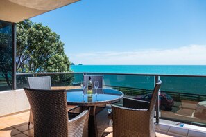 Un balcon agrémenté de meubles en osier, d’une table en verre et offrant une vue sur l’océan.