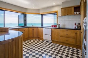 A kitchen with wooden cabinets, a checkered floor, a view of the sea, and a refrigerator. - Waterfront On Woolcombe - Spacious Holiday Home (New Plymouth)