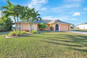 A single-story house with a sloped roof, a garage, and a well-maintained lawn with palm trees. - Western Sunsets-Heated Pool-Dock-Fresh Water Canal (Cape Coral)